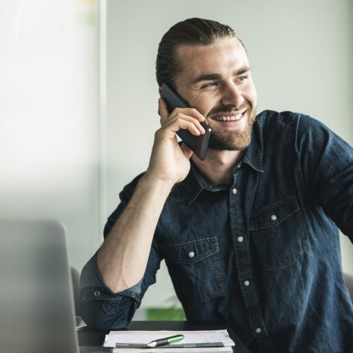 Smiling young businessman on cell phone in office